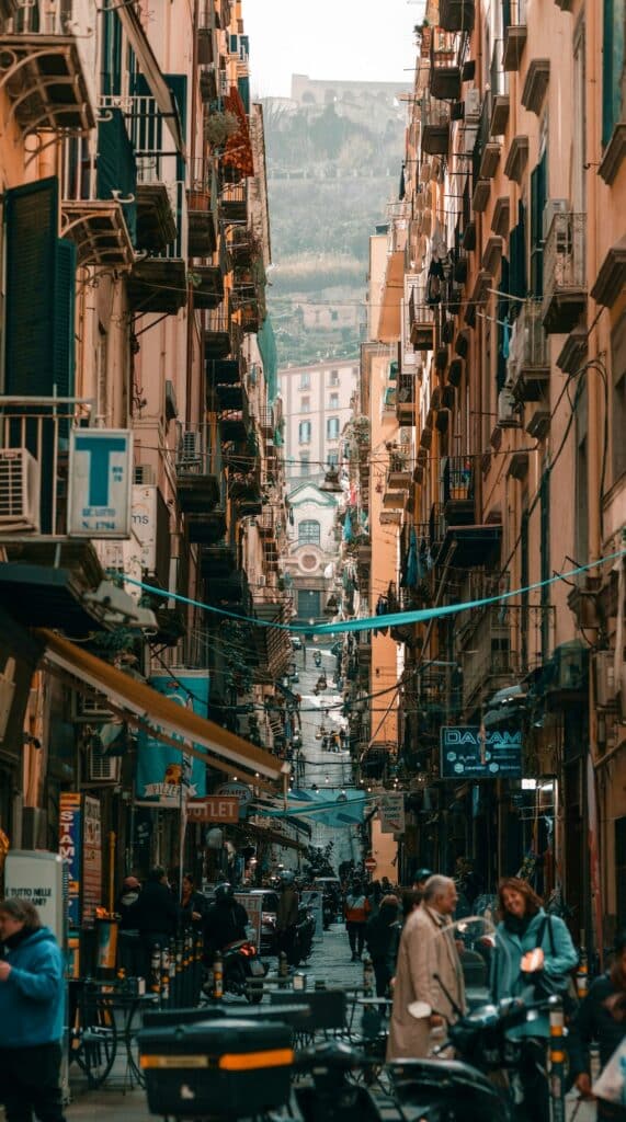 Una stretta strada di Napoli con edifici alti e persone che camminano